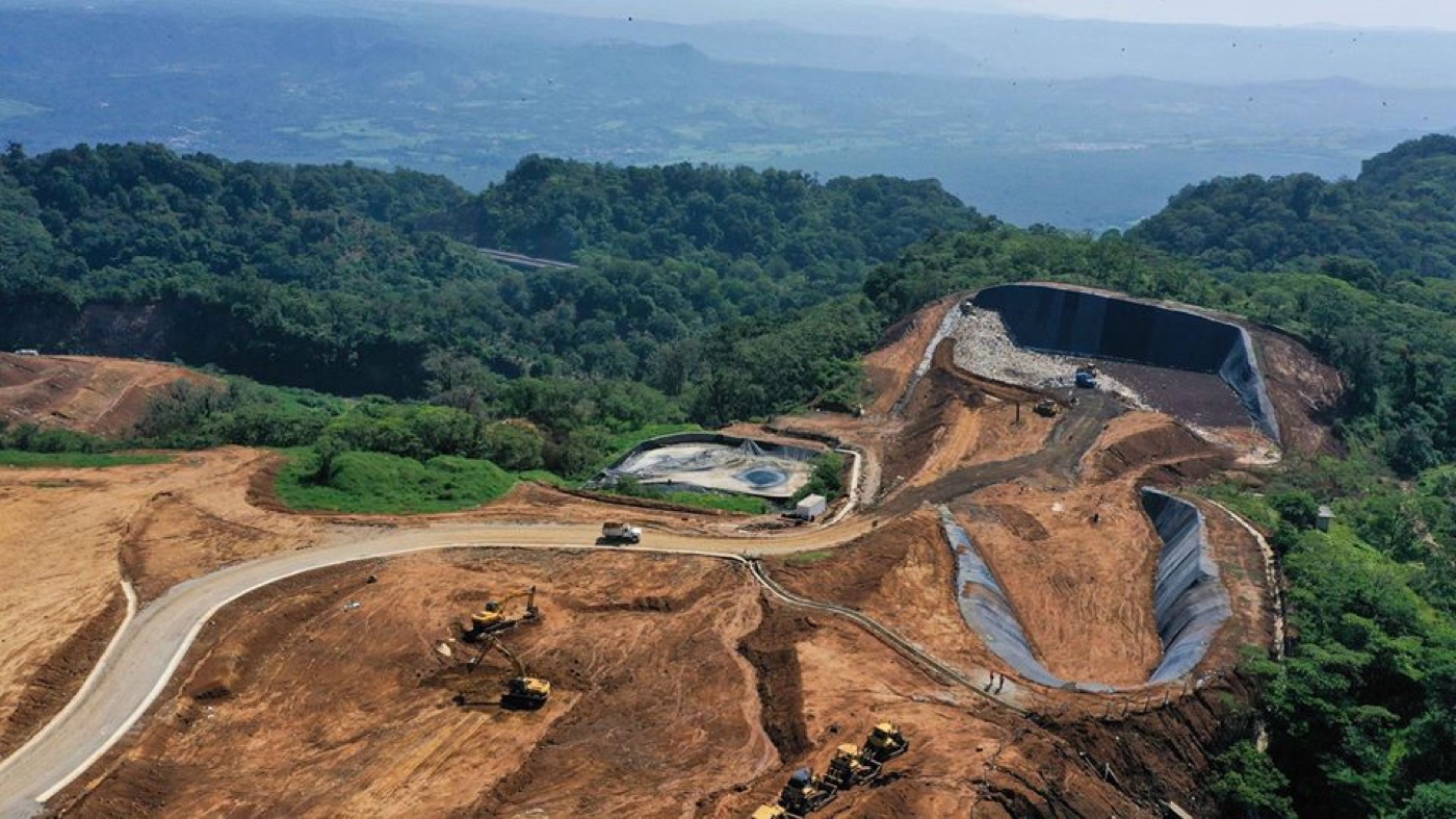 Vista aérea de un relleno sanitario en construcción, con celdas de geomembrana entre montañas